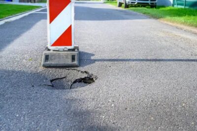 pothole on asphalt street with detour alert traffic sign