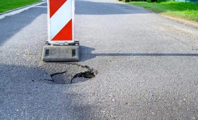 pothole on asphalt street with detour alert traffic sign